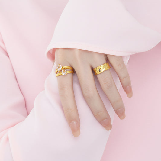 Hand wearing two gold rings on a plain background