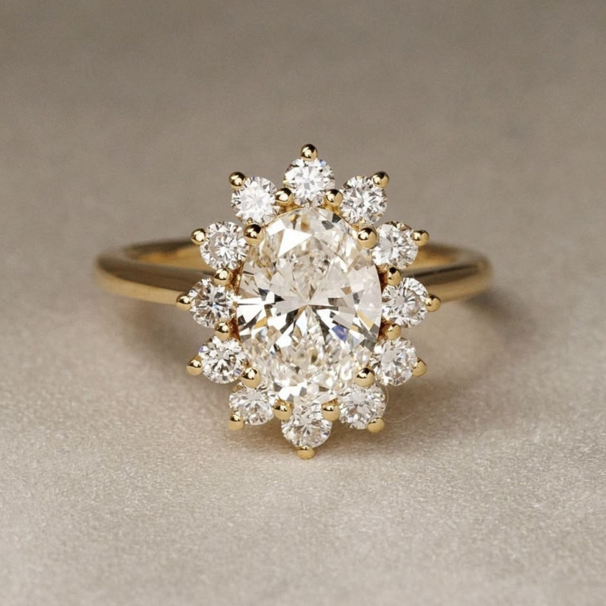 A yellow gold ring featuring a large oval center diamond surrounded by a halo of smaller round diamonds, set against a neutral textured beige background.