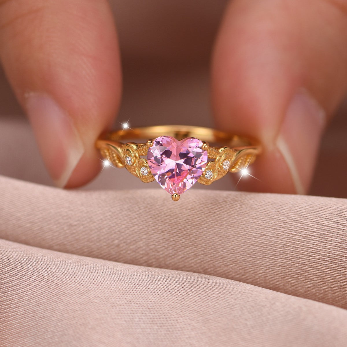 Gold ring with a pink heart-shaped gemstone held between fingers on a neutral background