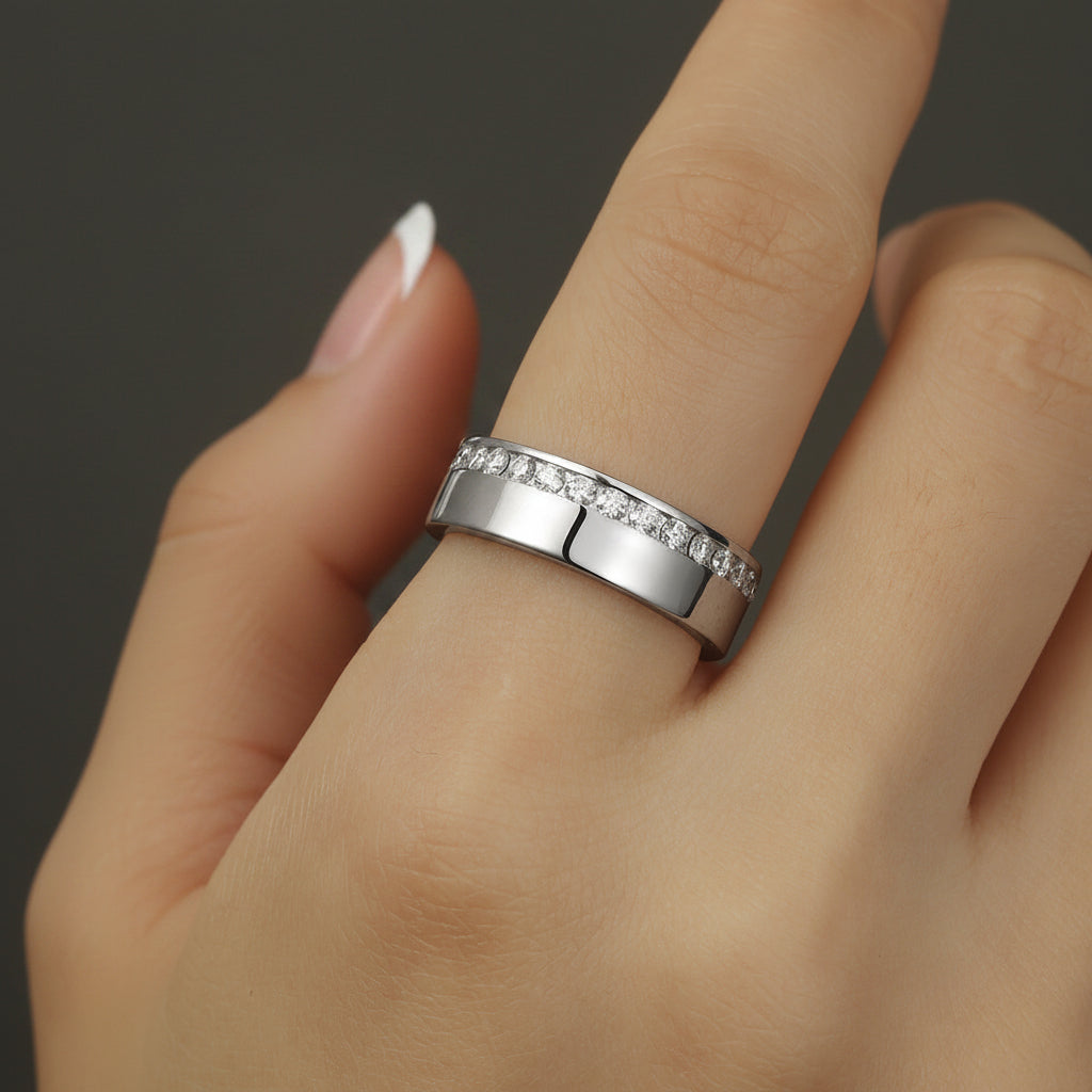 Silver ring with small diamonds on a finger against a dark background