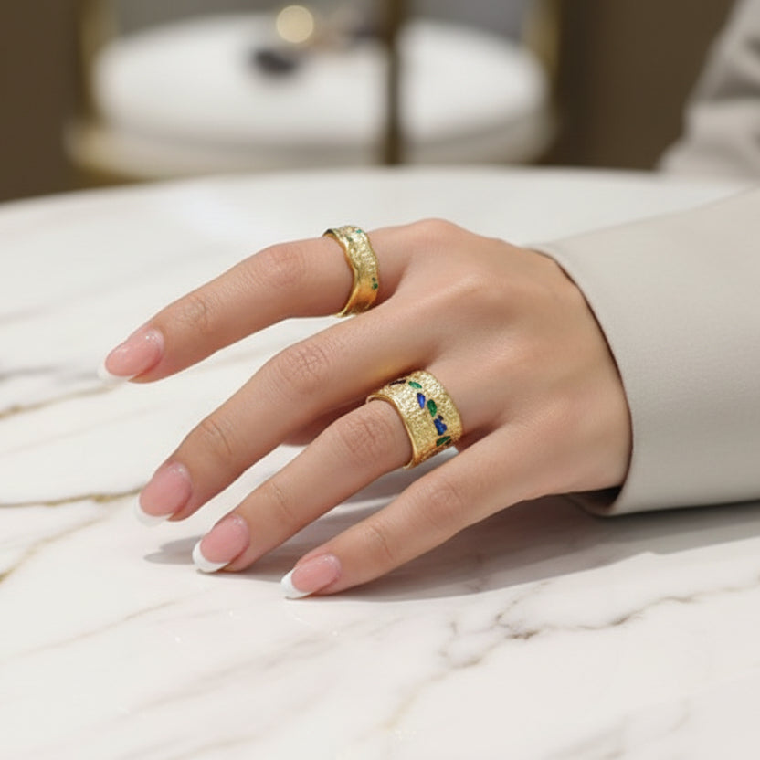 Hand with black nails and gold rings resting on a white surface.