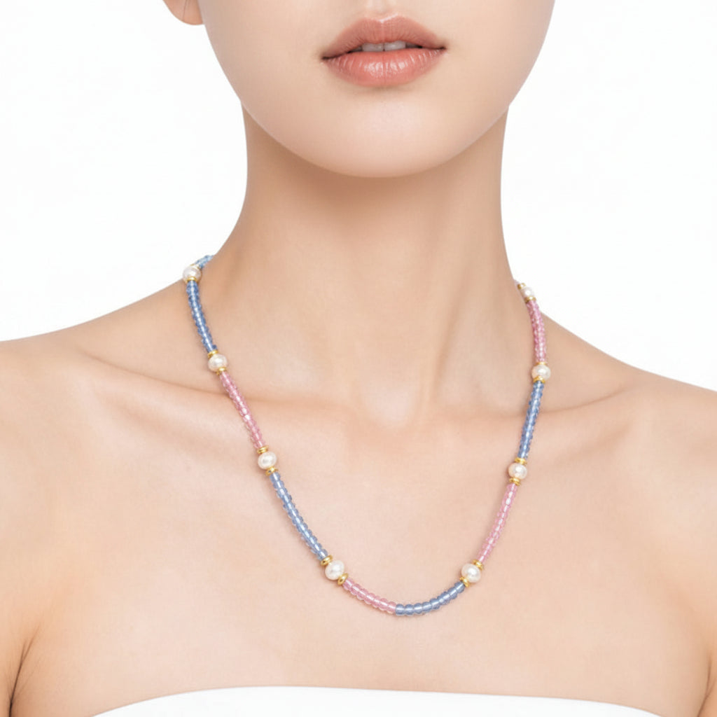 A close-up of a model wearing a delicate double-strand necklace made of alternating light blue and pink beads with small white pearl-like accents, set against a clean white background.