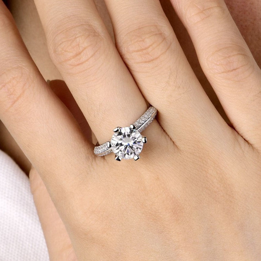A close-up of a hand wearing a silver-toned solitaire engagement ring with a round clear gemstone.