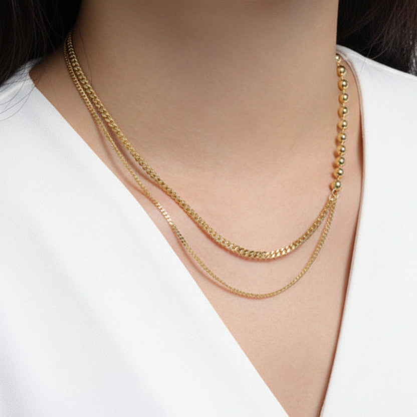 Person wearing two gold necklaces on a white shirt.