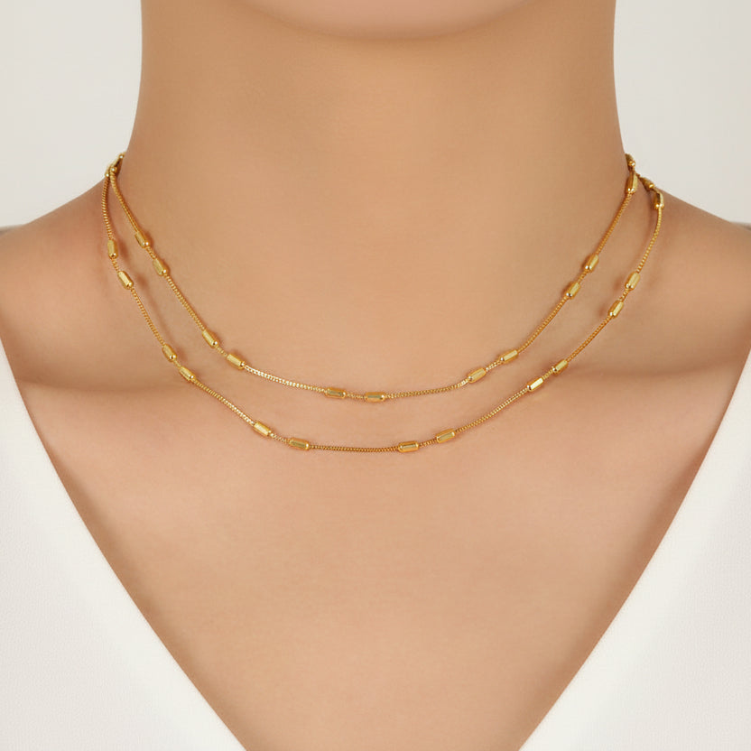 Layered gold necklaces on a model's neck with a white top.