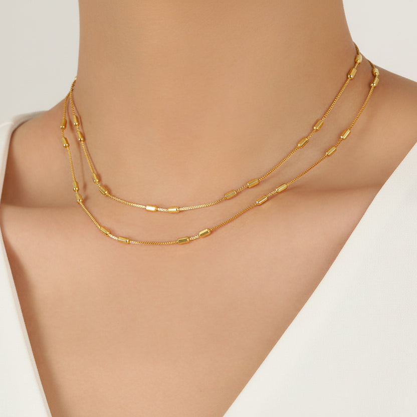Gold necklaces on a person's neck with a plain background