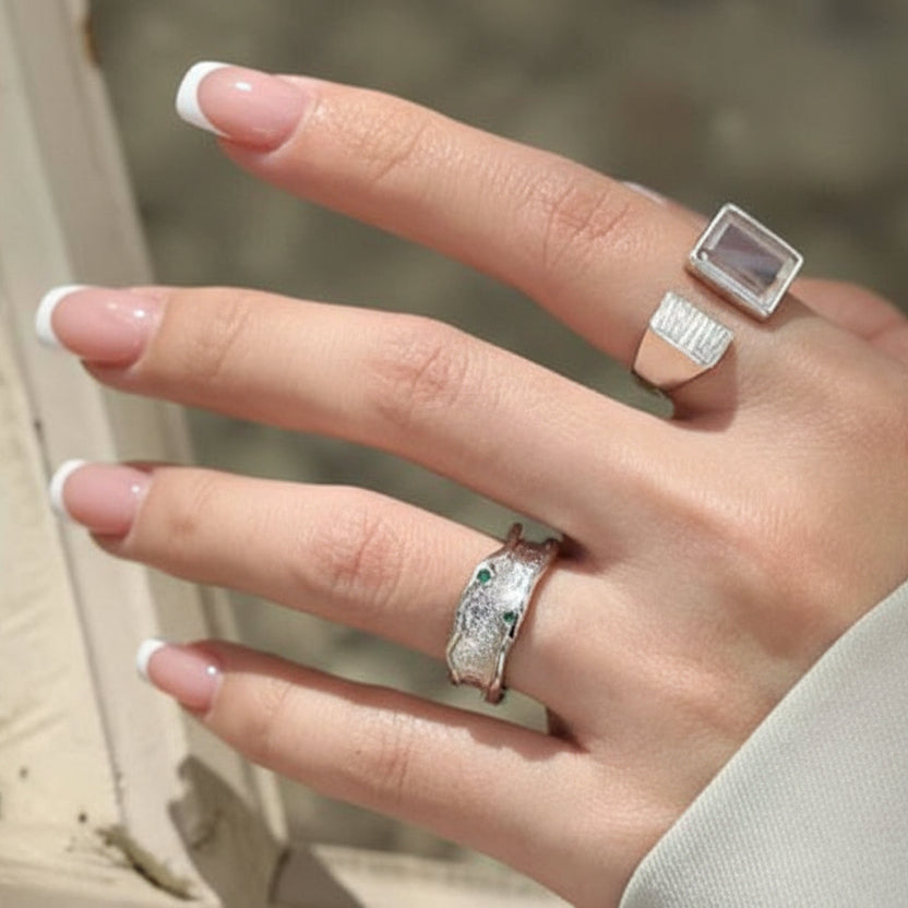 Hand with silver rings and black nail polish against a blurred background