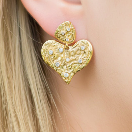 Gold heart-shaped earring worn on a person's ear with a blurred background