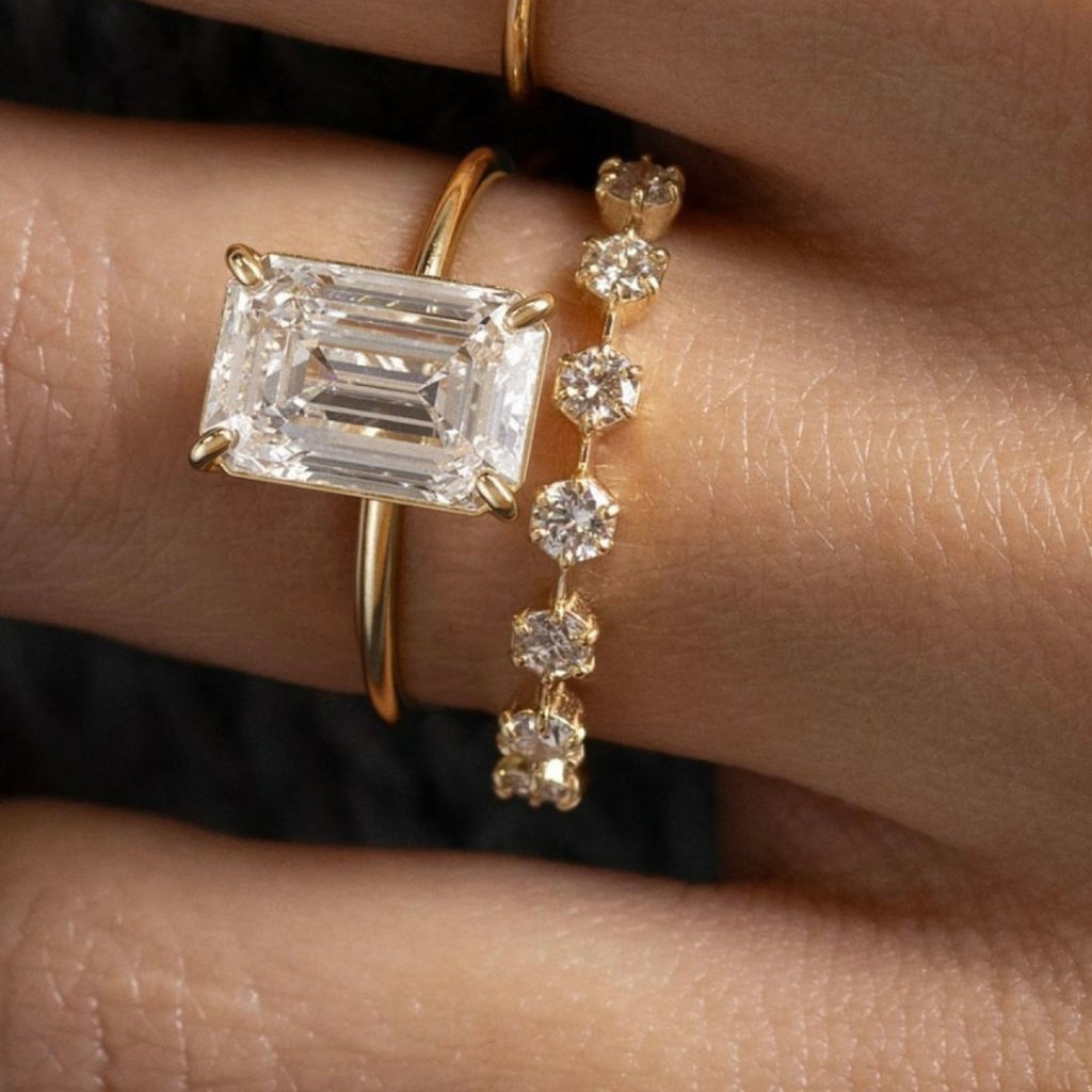 Gold ring with emerald-cut diamond and another gold ring with small diamonds on a hand.