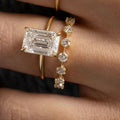 Gold ring with emerald-cut diamond and another gold ring with small diamonds on a hand.