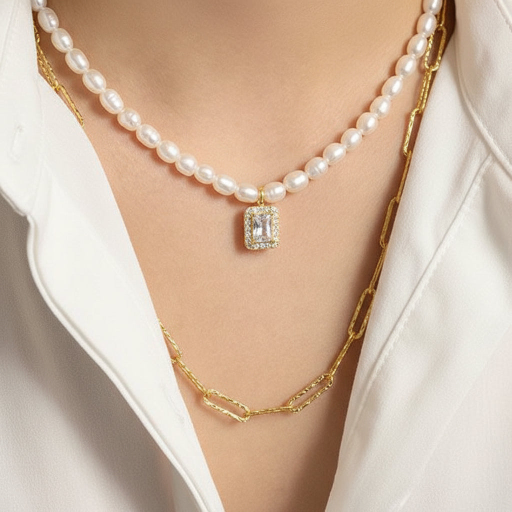 Pearl necklace with a diamond pendant worn by a person, with a gold chain necklace visible.