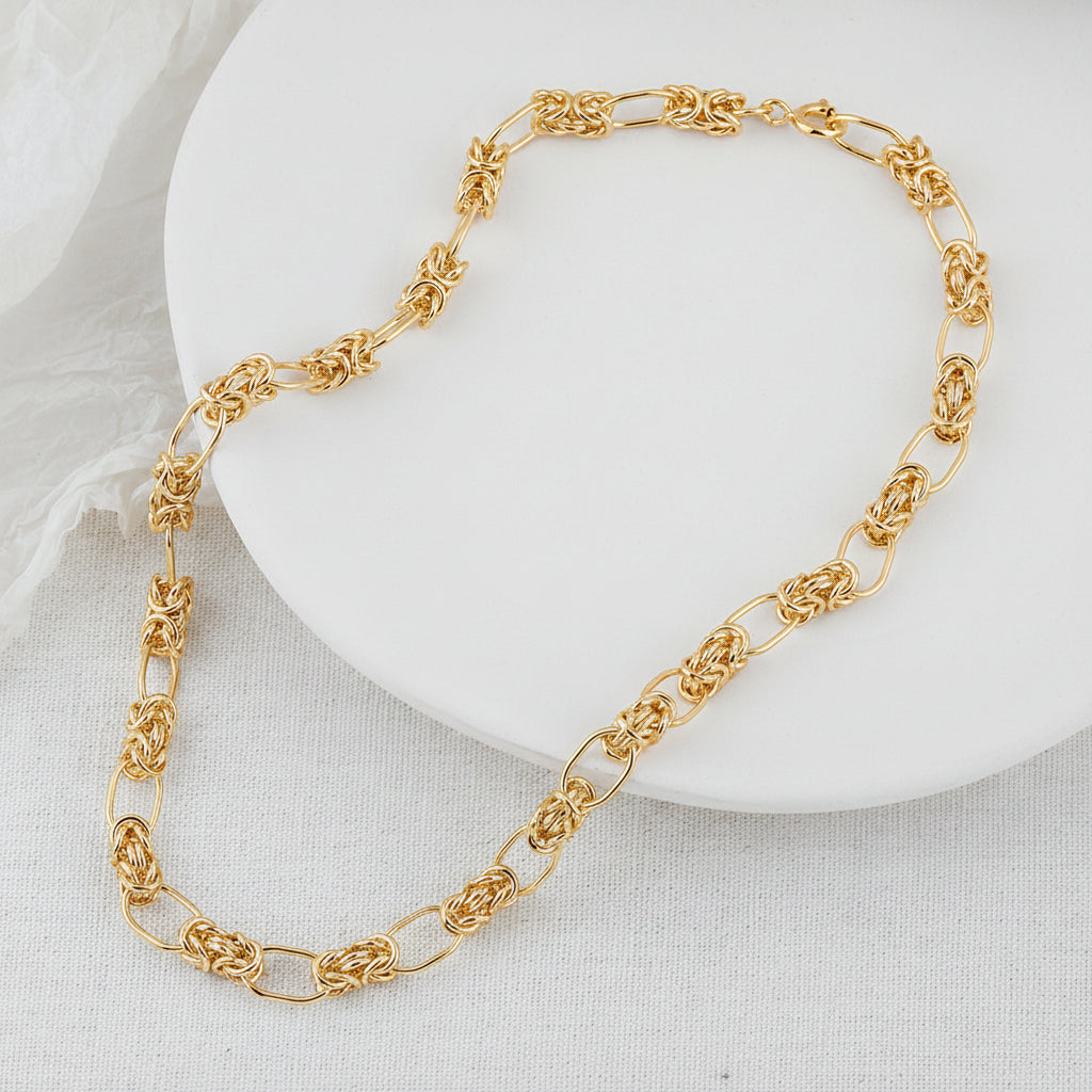 Gold chain necklace on a beige plate with a beige fabric background