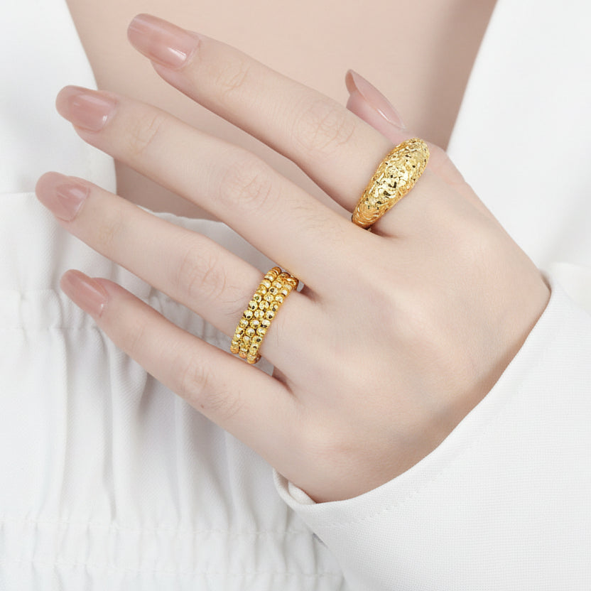 A person's hand showcasing two 925 sterling silver rings with an 18K yellow gold finish on a textured surface.
