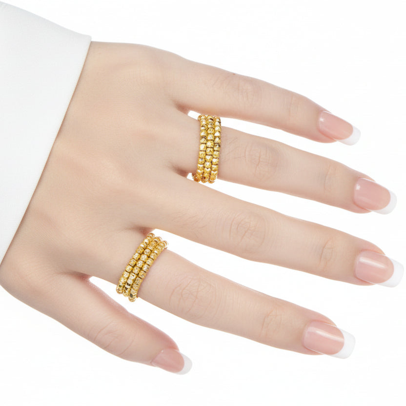 A person's hand wearing two 925 sterling silver rings with a rhombus bead design, one in an 18K yellow gold finish and the other in a rhodium finish.