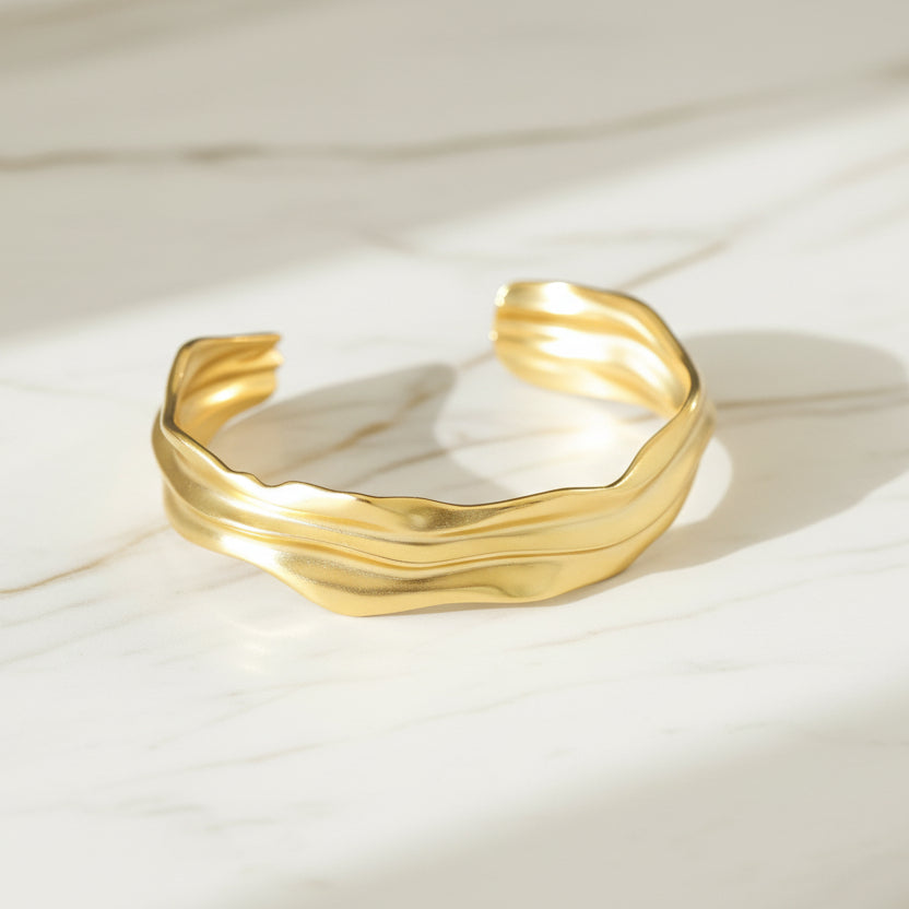 A gold-coloured open bangle bracelet with irregular folds, lalors jewellery