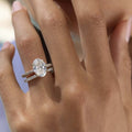 A close-up of a hand wearing an oval-cut diamond engagement ring with a matching pavé band in a silver-toned setting.