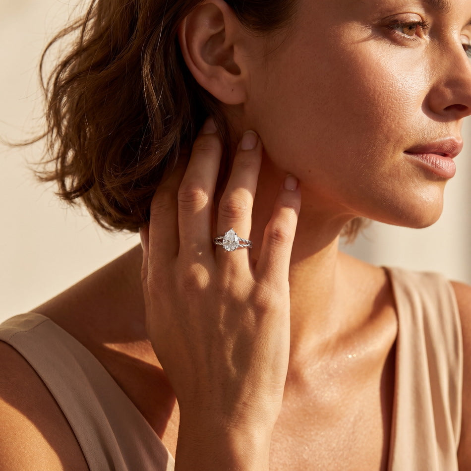 A close-up lifestyle shot of a woman wearing a silver-toned ring with a marquise-cut clear gemstone on her finger, set against a warm beige background.