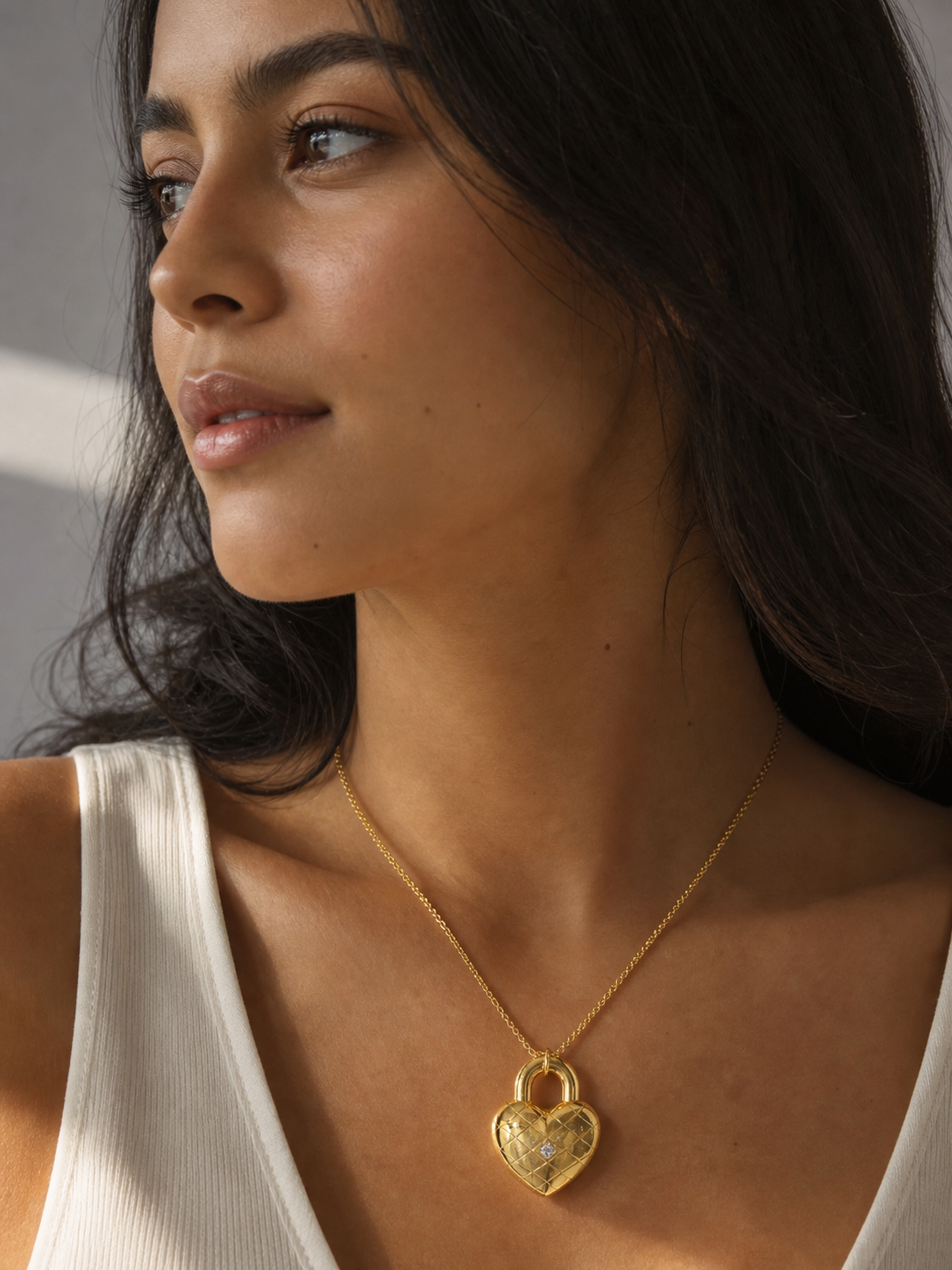 Woman wearing a gold necklace with a heart pendant against a neutral background