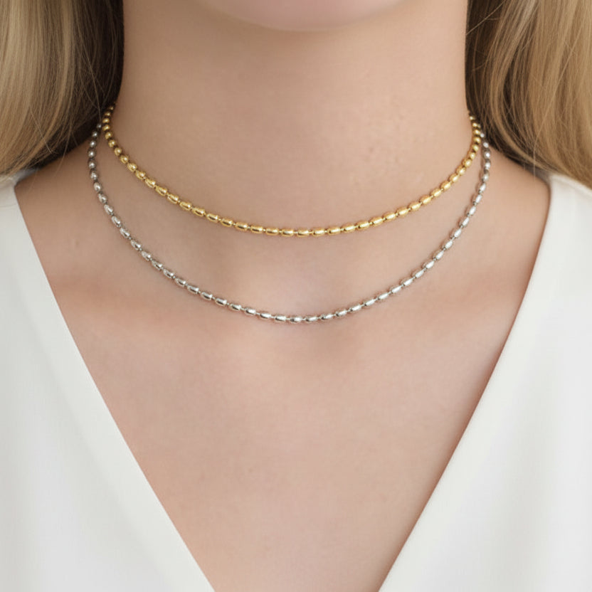 Two necklaces on a person's neck, one gold and one silver, against a white background.