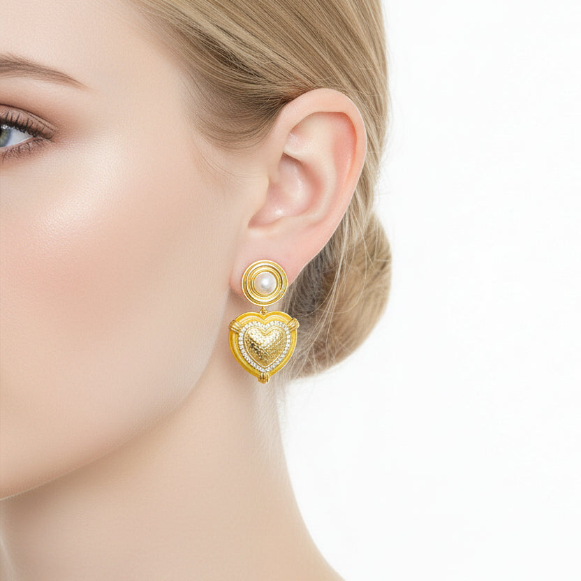 Gold heart-shaped earrings worn by a person on a white background