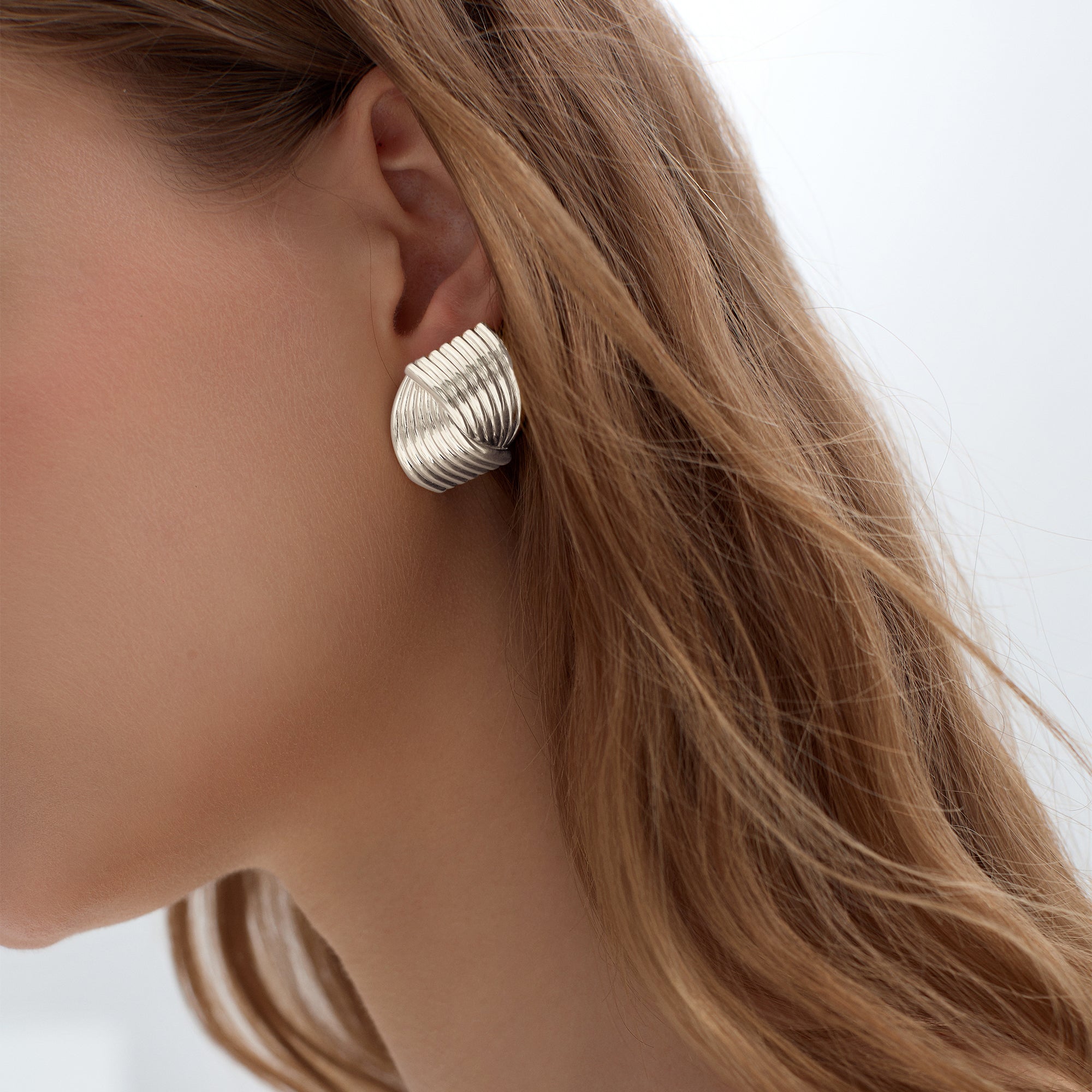 Close-up of a woman wearing a silver textured earring with a blurred background