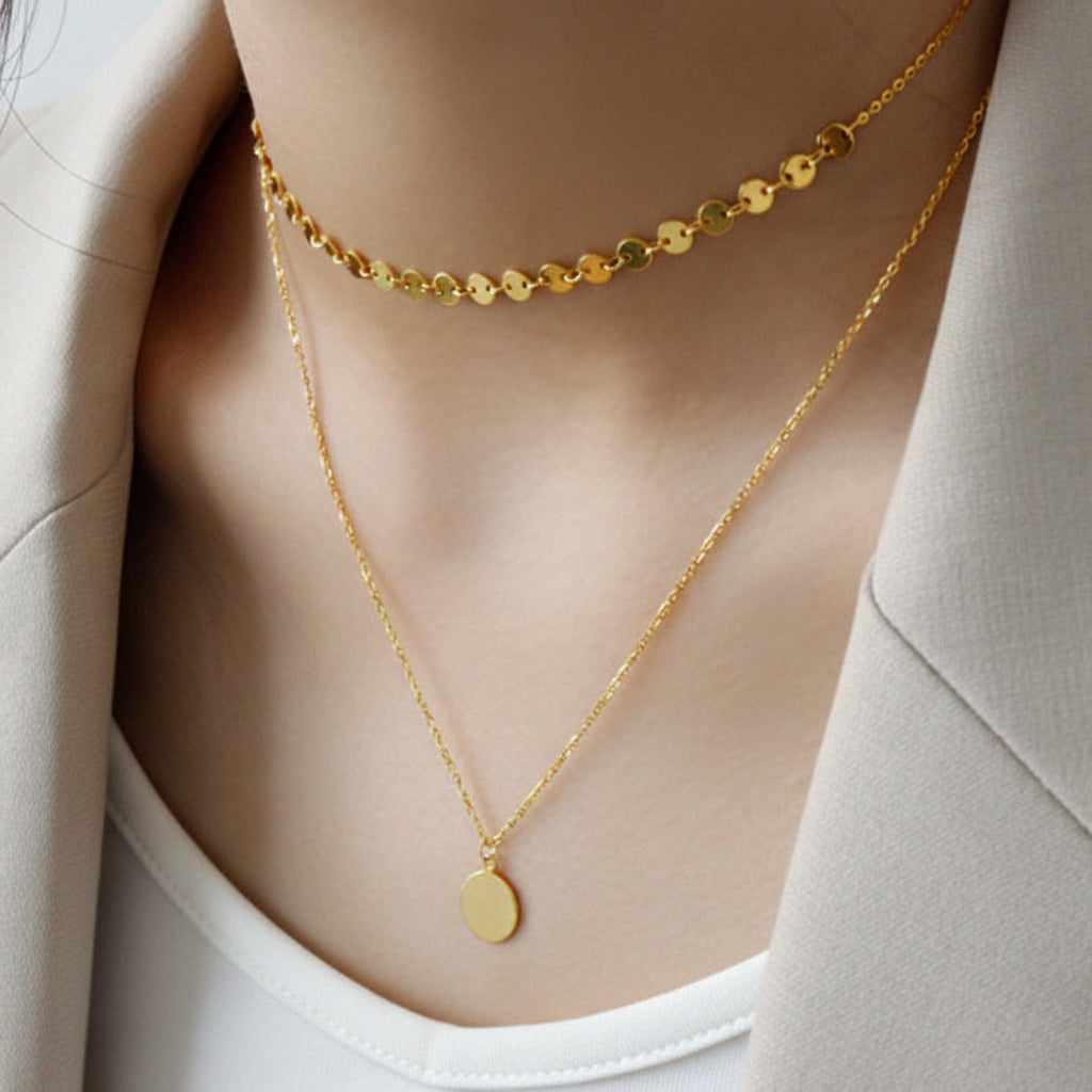 Person wearing double layer choker gold necklaces on a neutral background