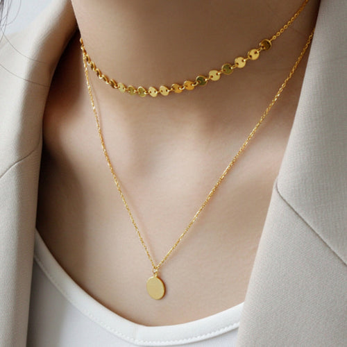 Person wearing double layer choker gold necklaces on a neutral background