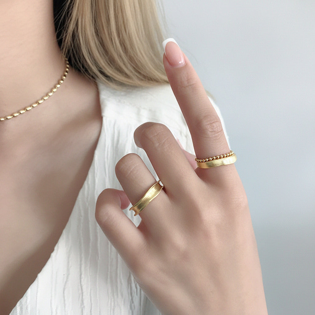 Close-up of a hand wearing gold rings with a neutral background