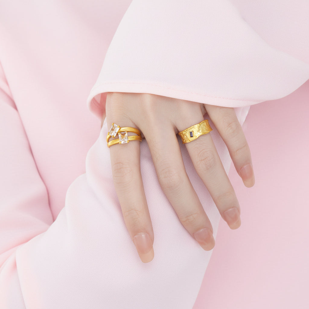 Hand wearing two gold rings on a plain background