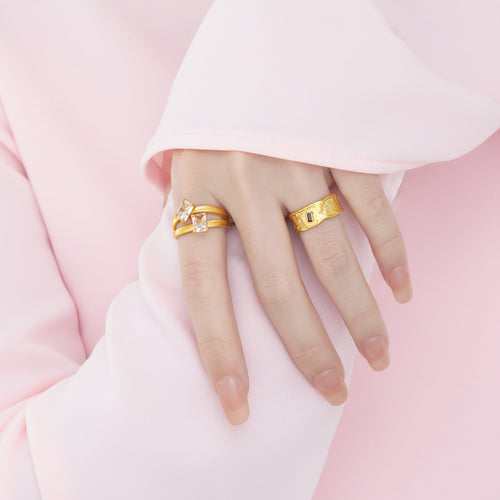 Hand wearing two gold rings on a plain background