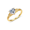 A yellow gold ring featuring a heart-shaped clear gemstone in a prong setting, accented by two small round diamonds on the shoulders, shown on a clean white background.