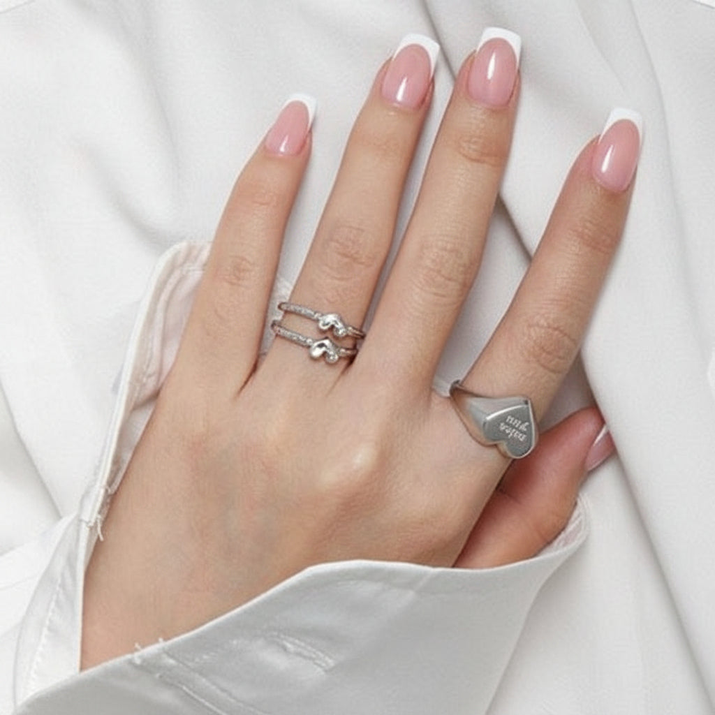 Hand with black nail polish and silver rings on a white fabric background