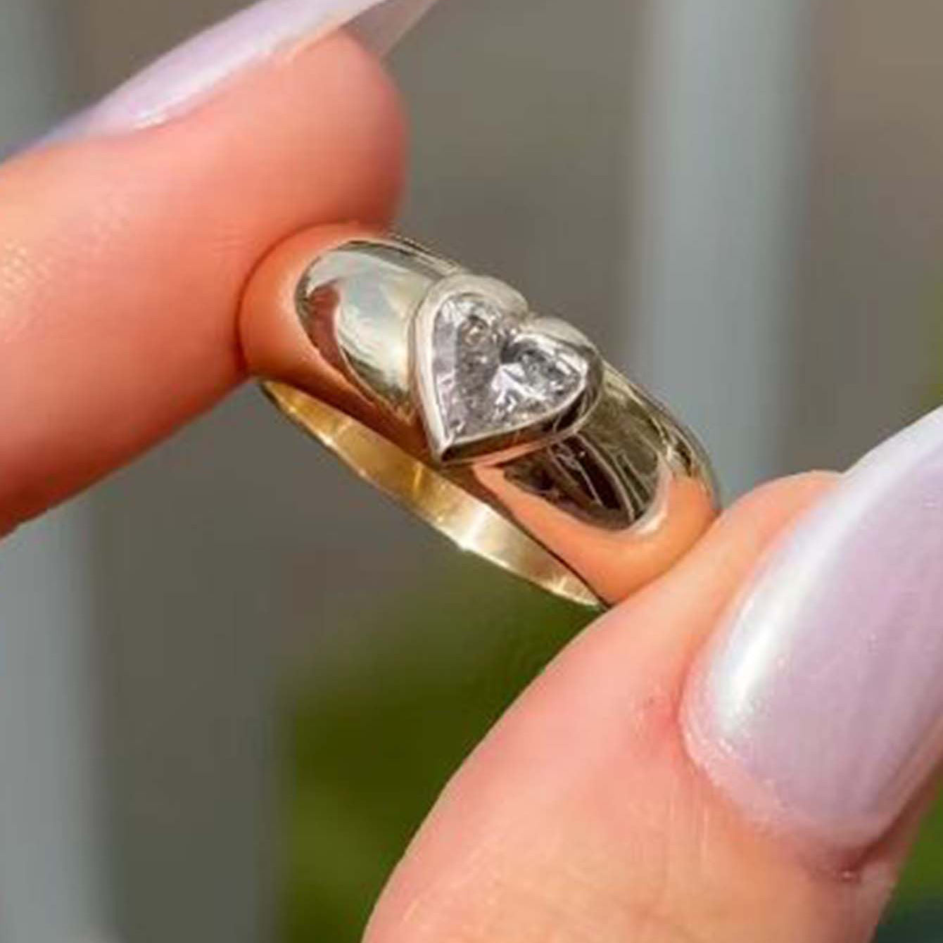Gold ring with heart-shaped diamond on a finger against a blurred background