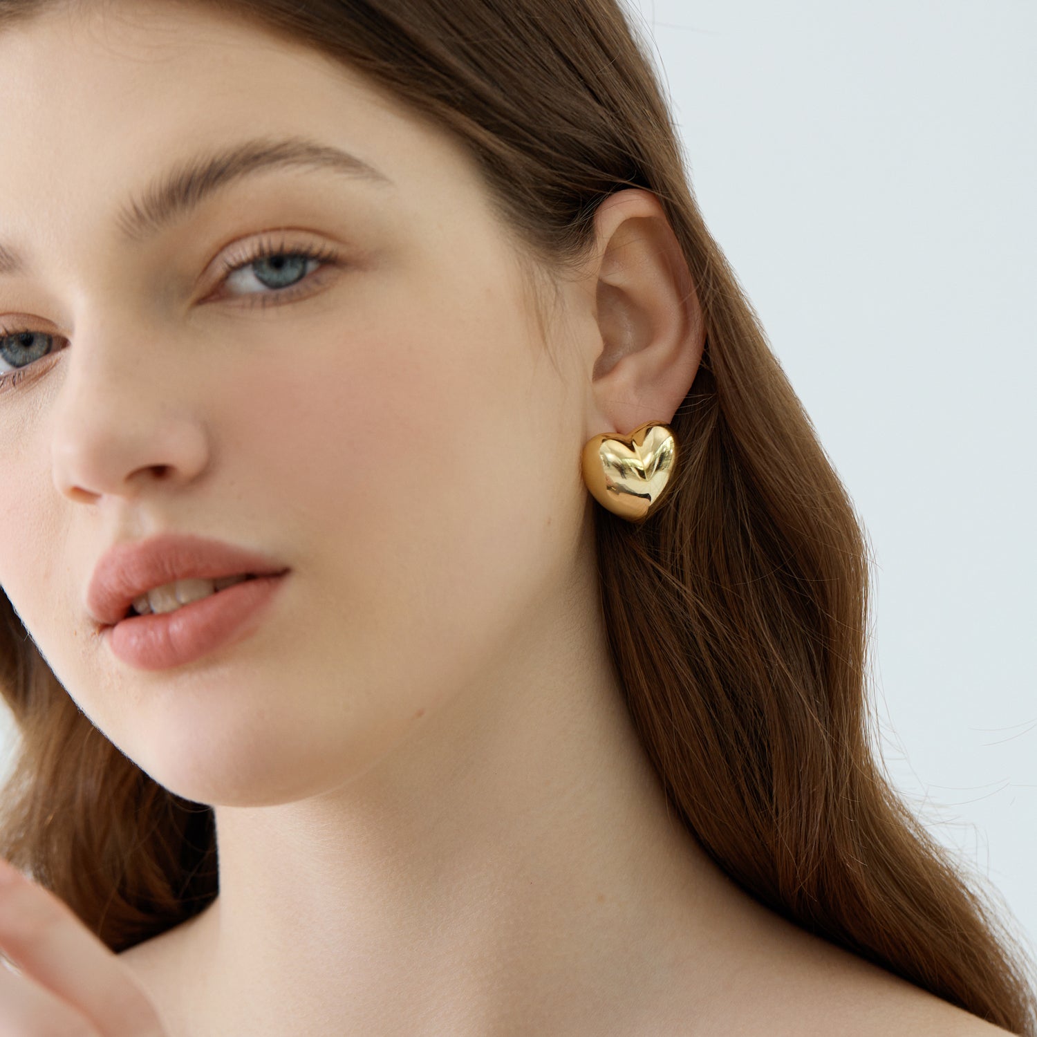 A person wearing a large heart-shaped stud earring made of 999 pure silver with an 18K yellow gold finish.