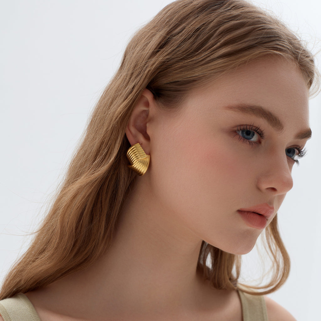 Woman wearing gold leaf-shaped earrings against a neutral background