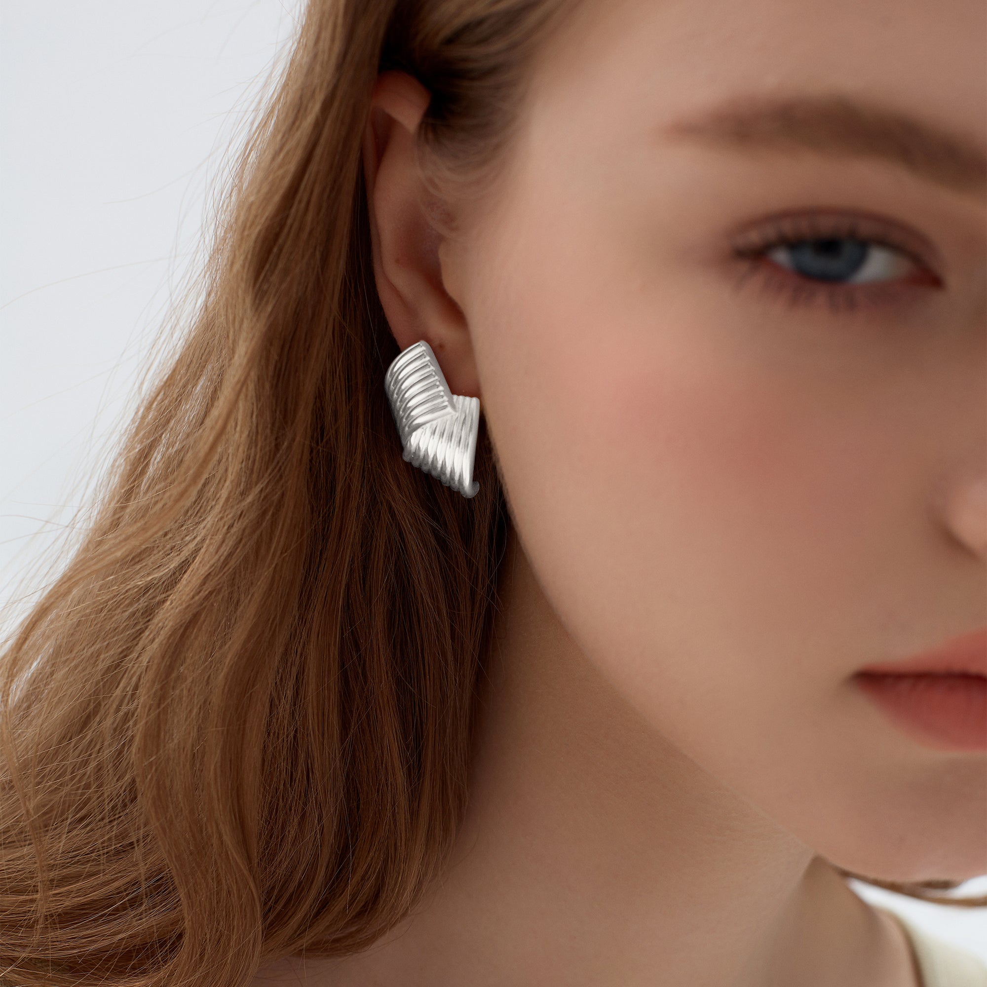 Close-up of a person wearing a silver earring with a neutral background