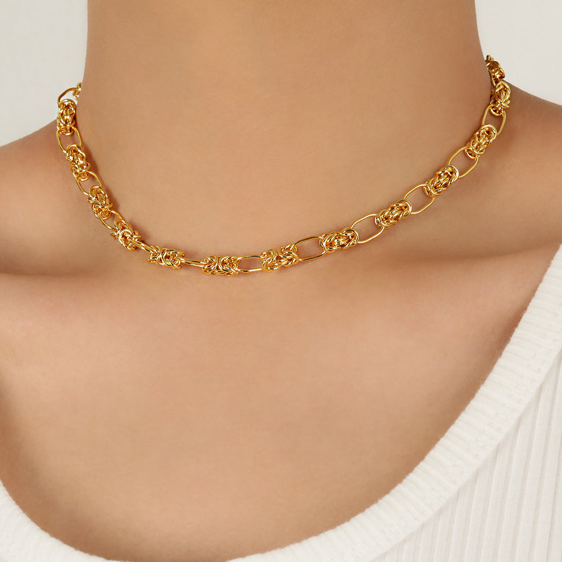 Gold chain necklace on a person wearing a white top against a neutral background