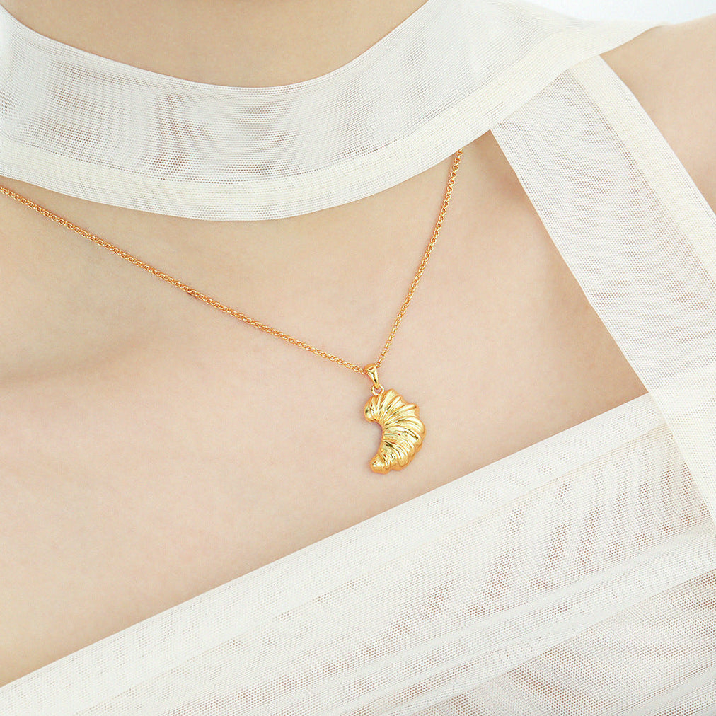 Gold necklace with a pendant worn by a person in a white outfit.