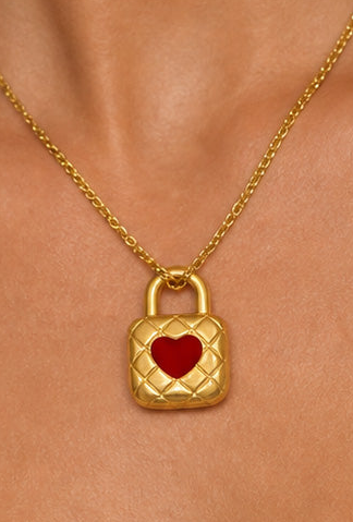A gold necklace with a padlock-shaped pendant featuring a red heart in the center, worn on a model's neck.