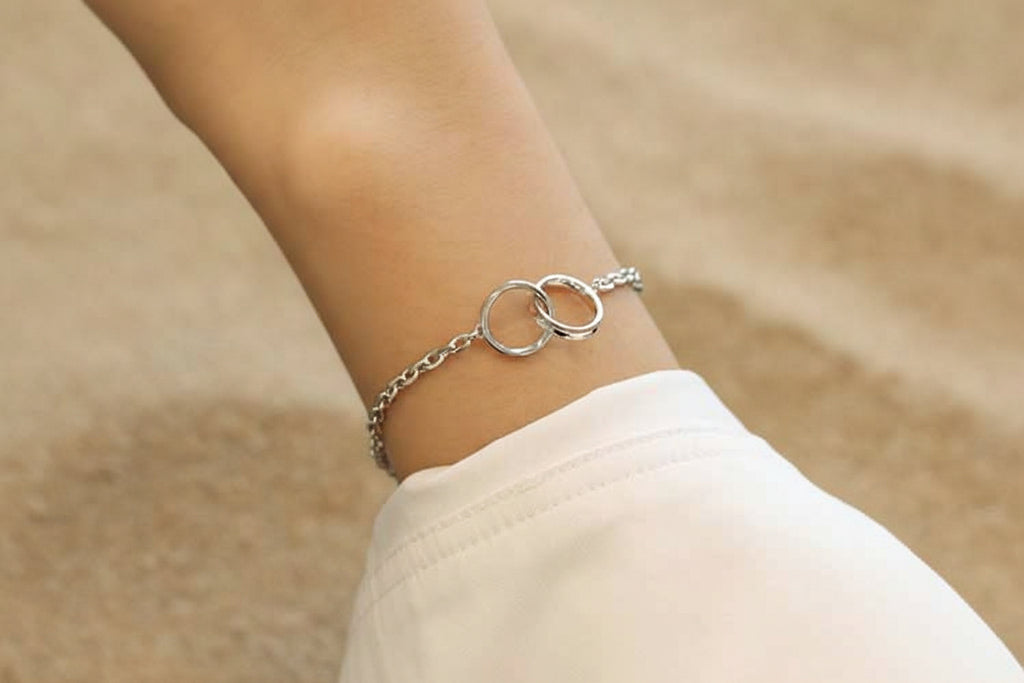 Silver bracelet with interlocking rings on a wrist against a neutral background