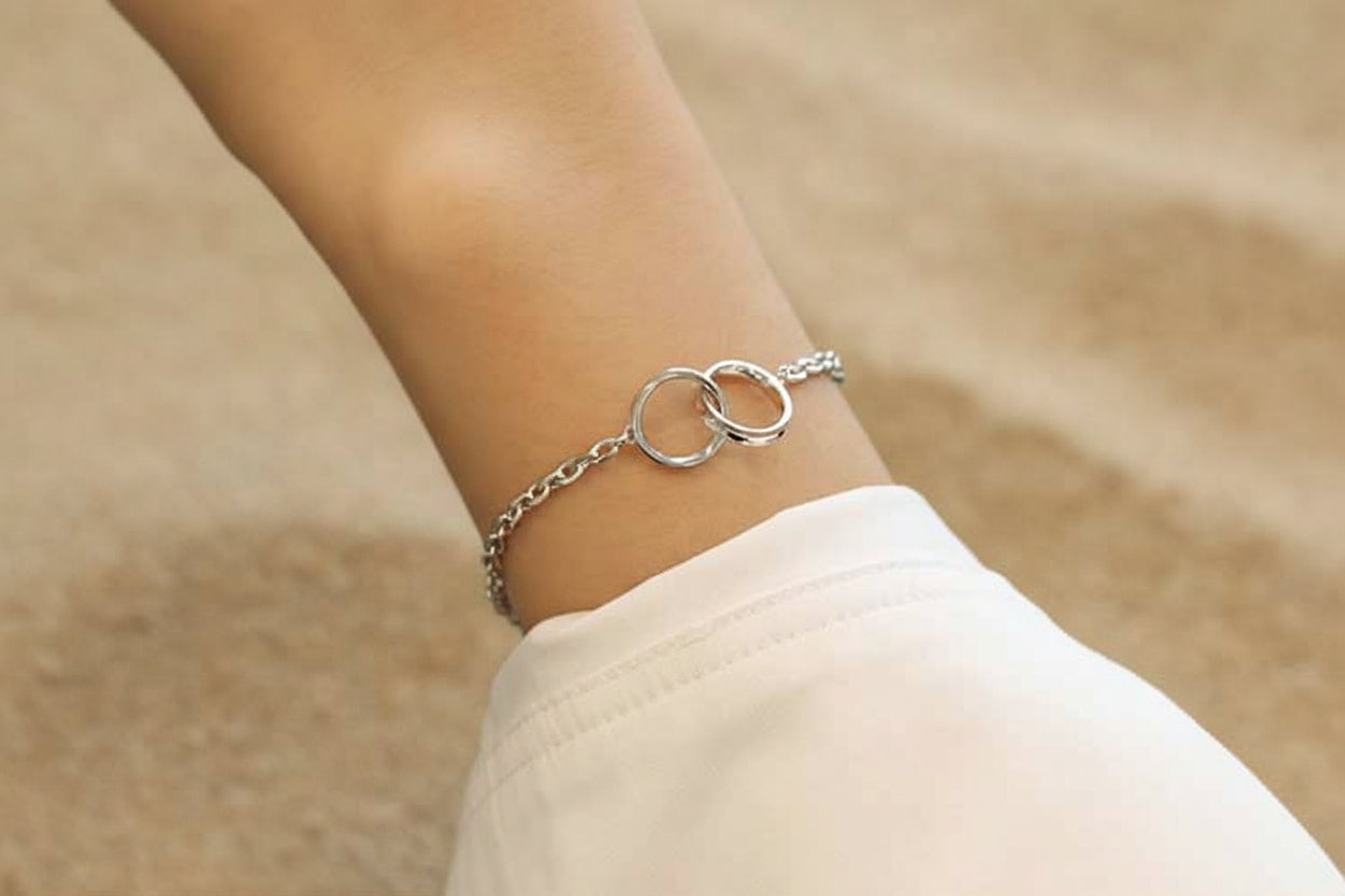 Silver bracelet with interlocking rings on a wrist against a neutral background